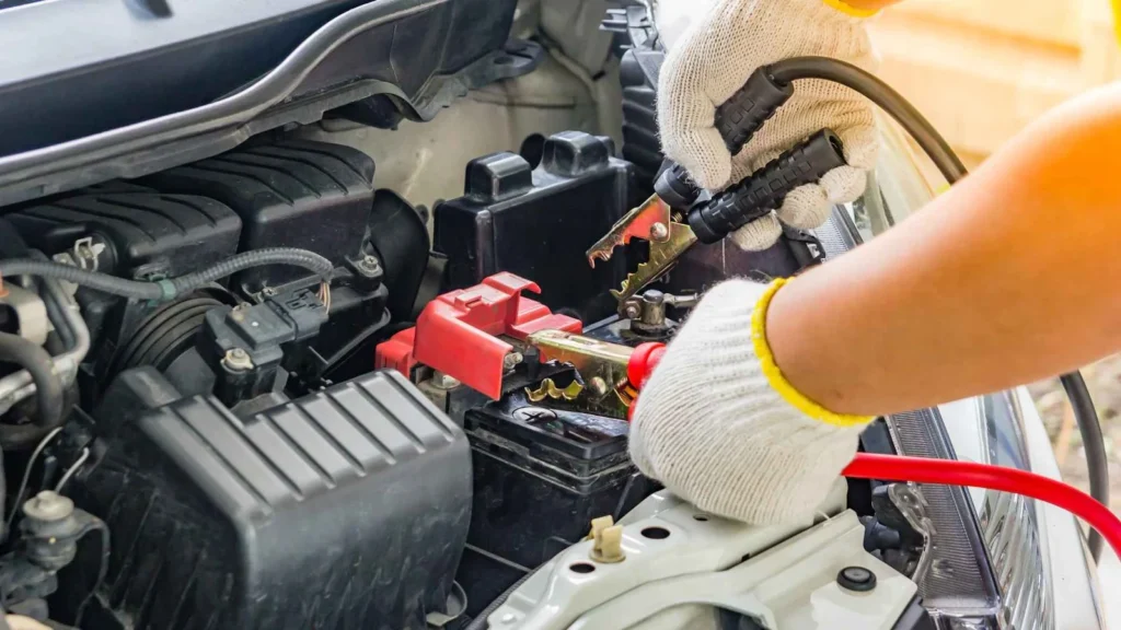 a person holding a jumper cable to a car battery